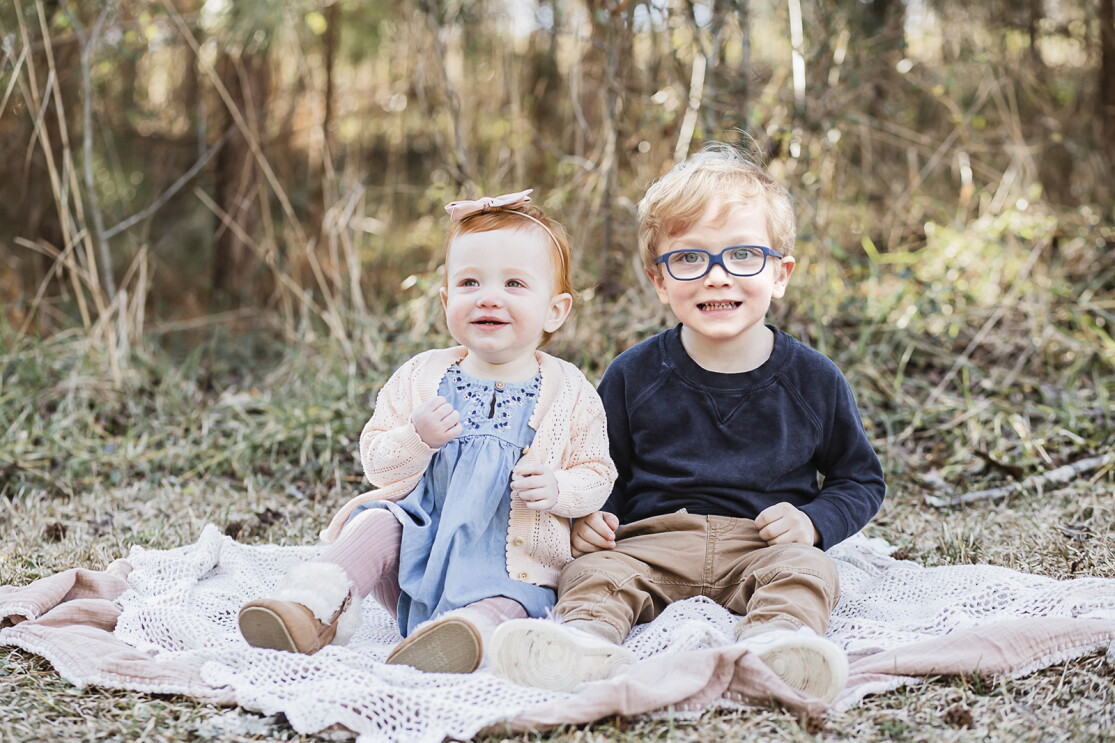 An image of two children sitting on a blanket outside smiling for a professional photo.