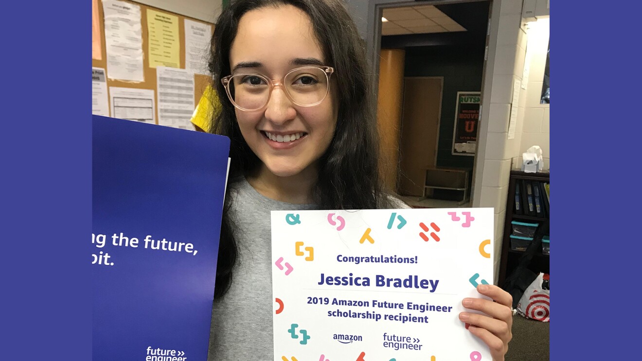 A young woman who is a high school senior smiles at the camera and shows her 2019 Amazon future engineer scholarship award announcement.