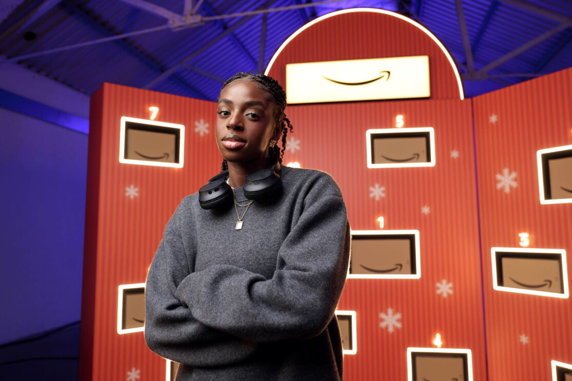Cat Burns wearing headphones around her neck, stood in front of a giant advent calendar with Amazon boxes
