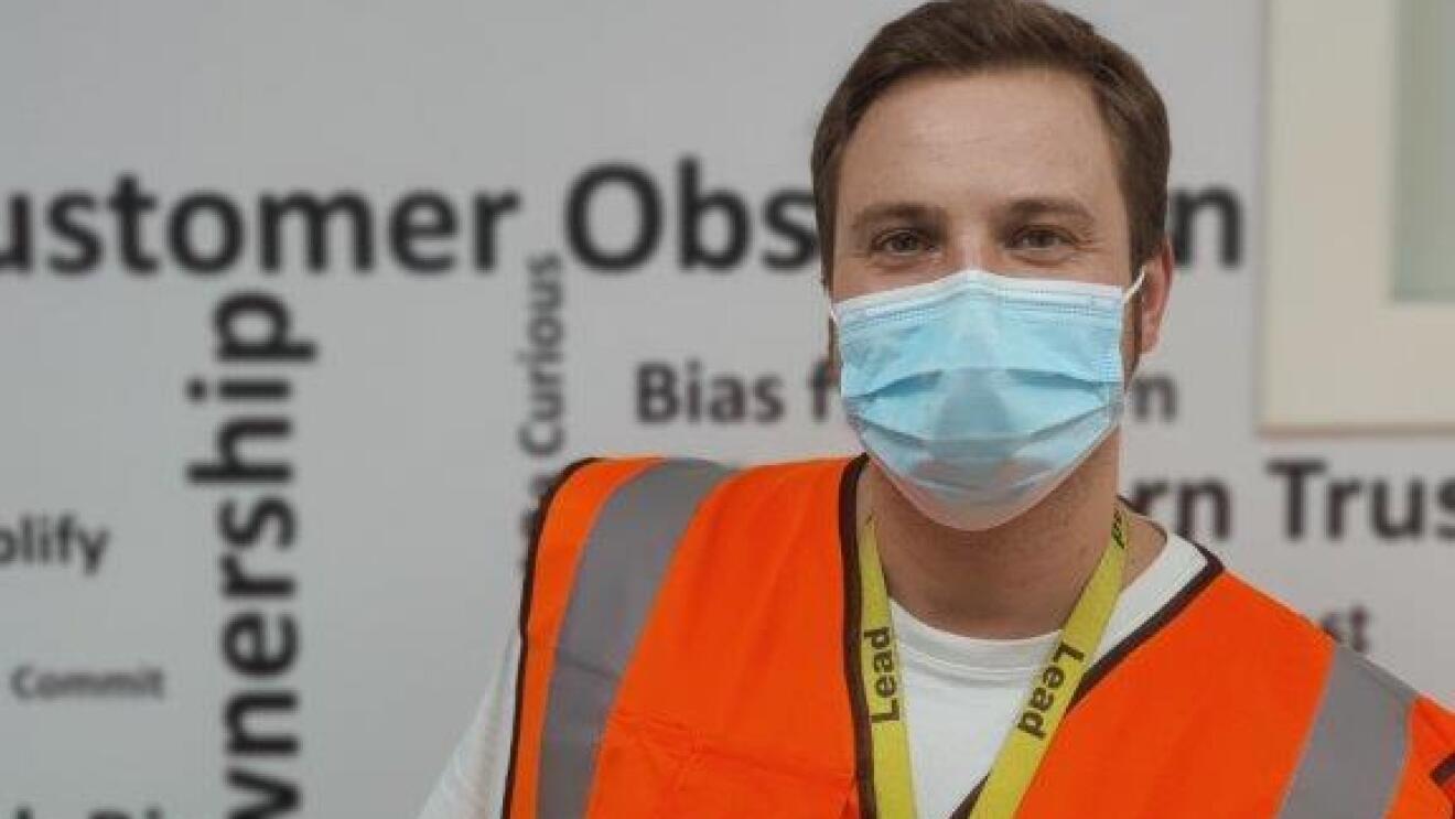 Ein junger Mann mit Maske und Sicherheitsweste.