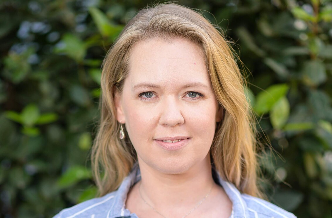 A headshot image of Donna Edwards. She is outside and there is a wall of greenery behind her.