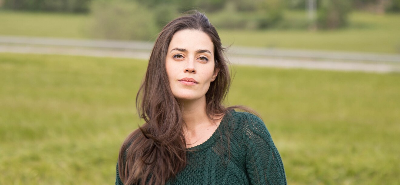 Lorena Franco es escritora y empezó autopublicándose en 2016 con el servicio KDP de Amazon. En un parque con fondo de árboles y césped está un plano corto de Lorena con el pelo castaño y muy largo y al viento. Tiene los ojos marrones azules y mira a cámara sin sonreir. Lleva un jersey de punto calado de color verde.