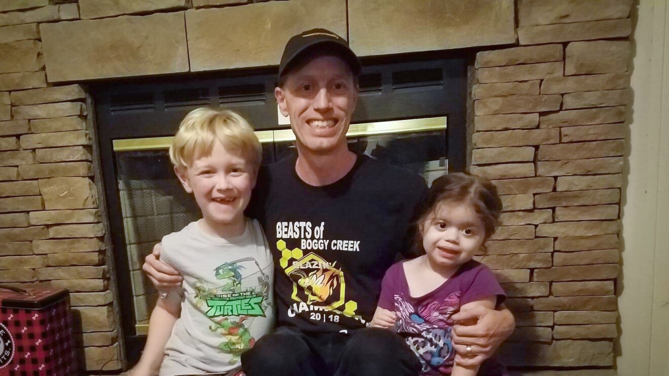 A man sits in front of a fireplace with two small kids.