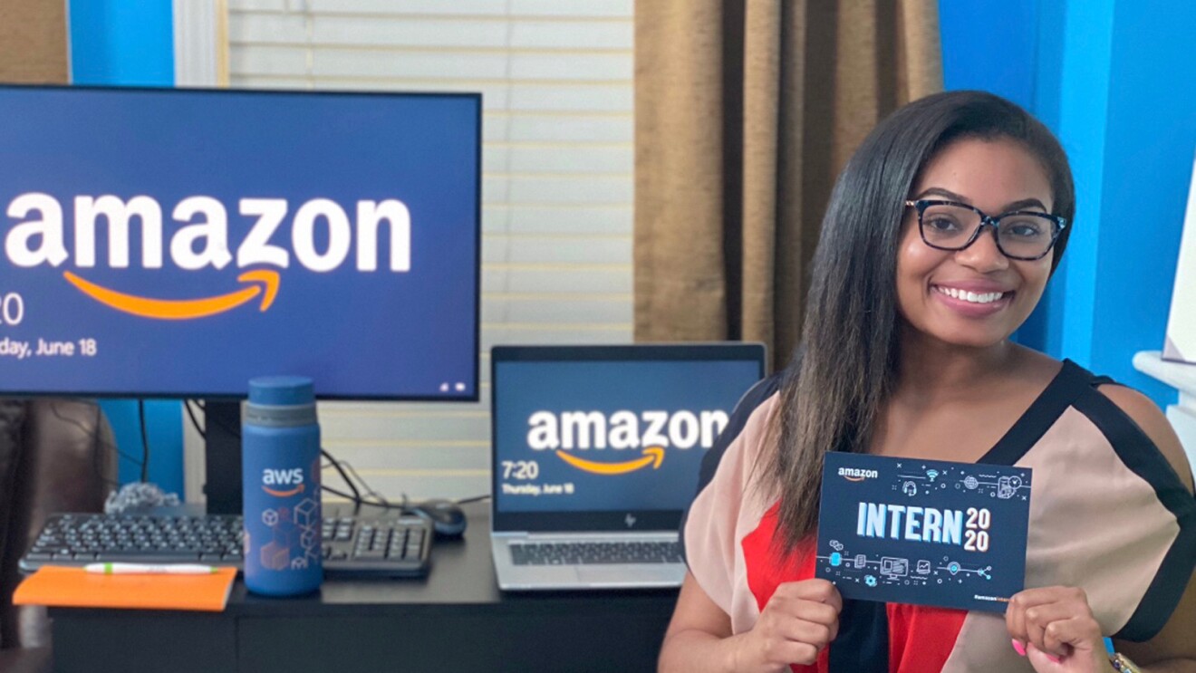 A woman sits in front of a desk. She holds a card that says "Amazon intern 2020."