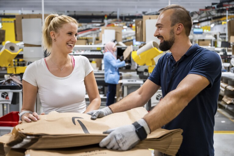 Eine Amazon Mitarbeiterin und ein Mitarbeiter an einer Packstation im Logistikzentrum.