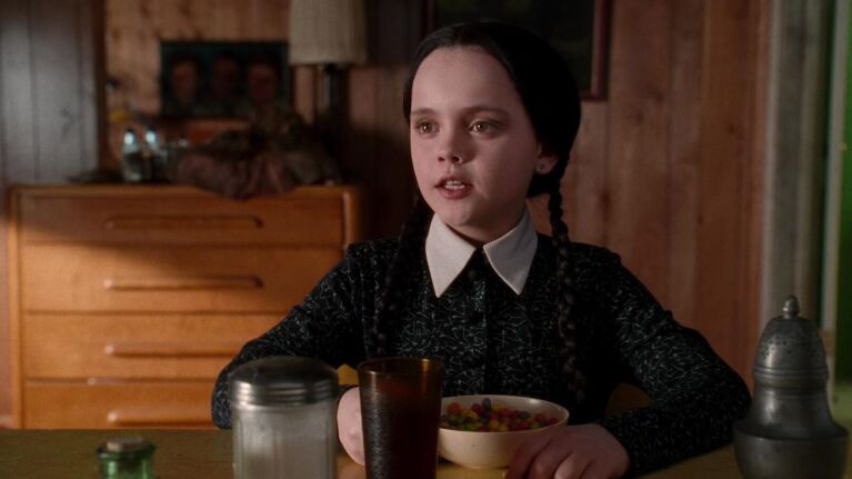 Wednesday Addams character seated for breakfast in wooden room