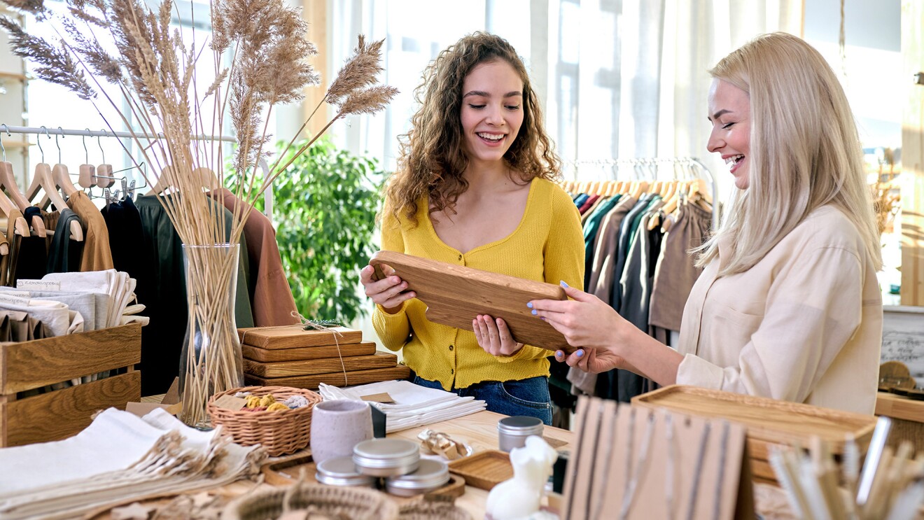 一个穿着黄色衬衫的女人和她旁边另一个穿着奶油色衬衫的女人的图片。他们在一家商店里一起看一件木制品。