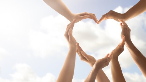 Image of various hands forming a heart, against a clear blue sky.
