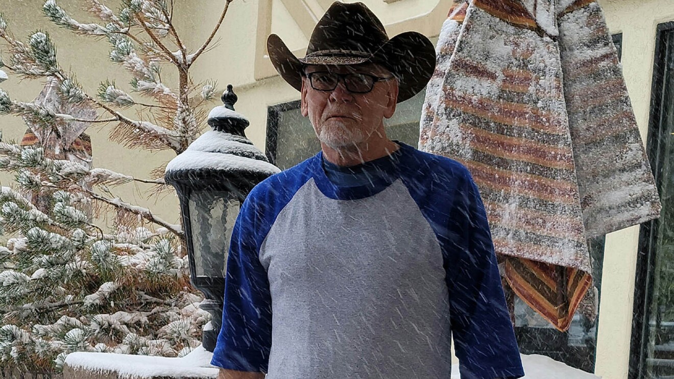 An image of a man standing for a photo outside in the snow wearing a cowboy hat.