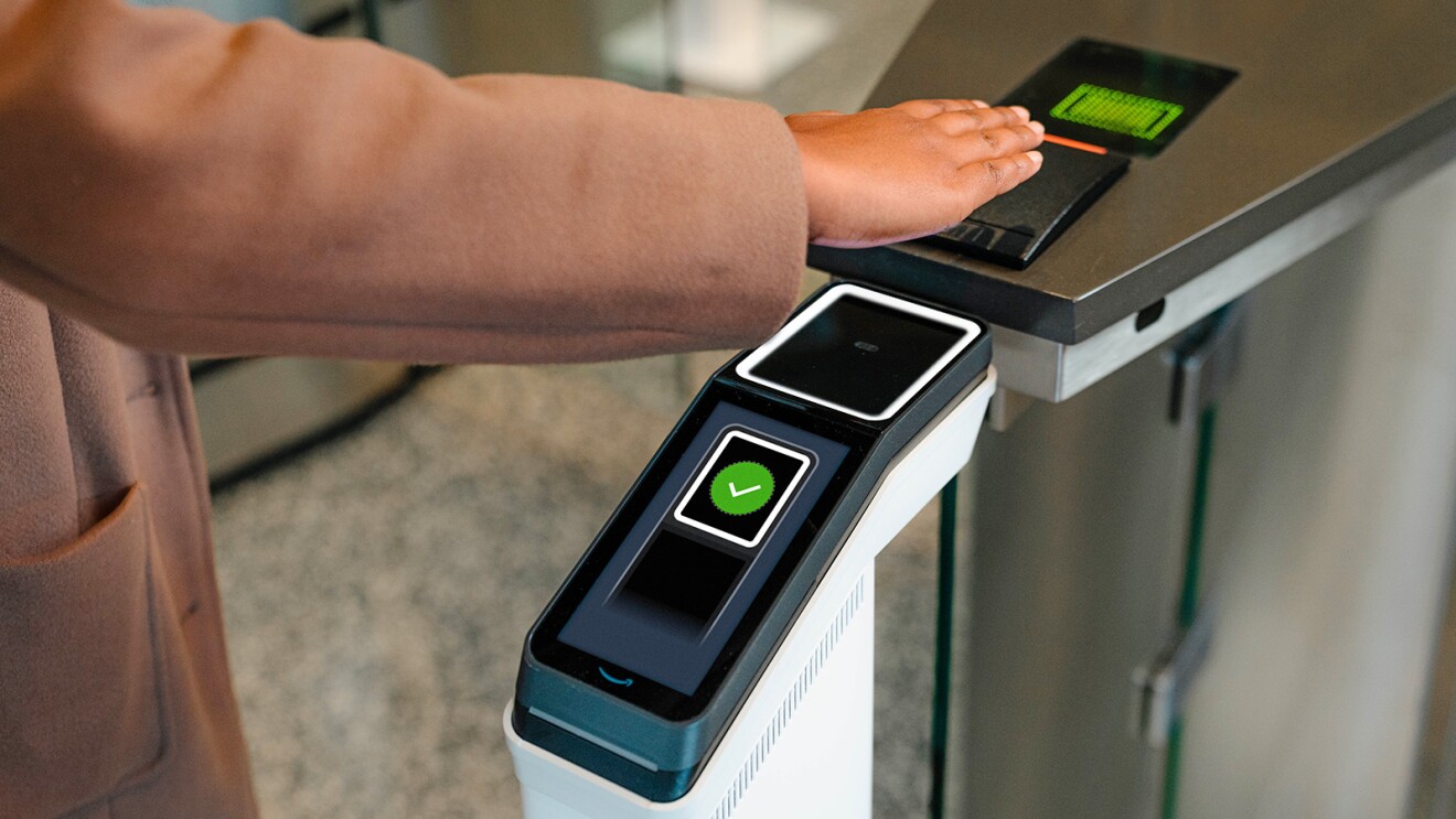 A photo of an employee walking into an office, and entering a security gate using Amazon One palm recognition technology.