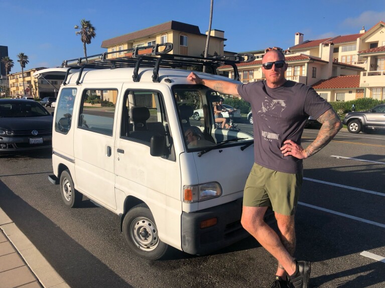 Josh Palacios leans on the front of a white van parked outside.