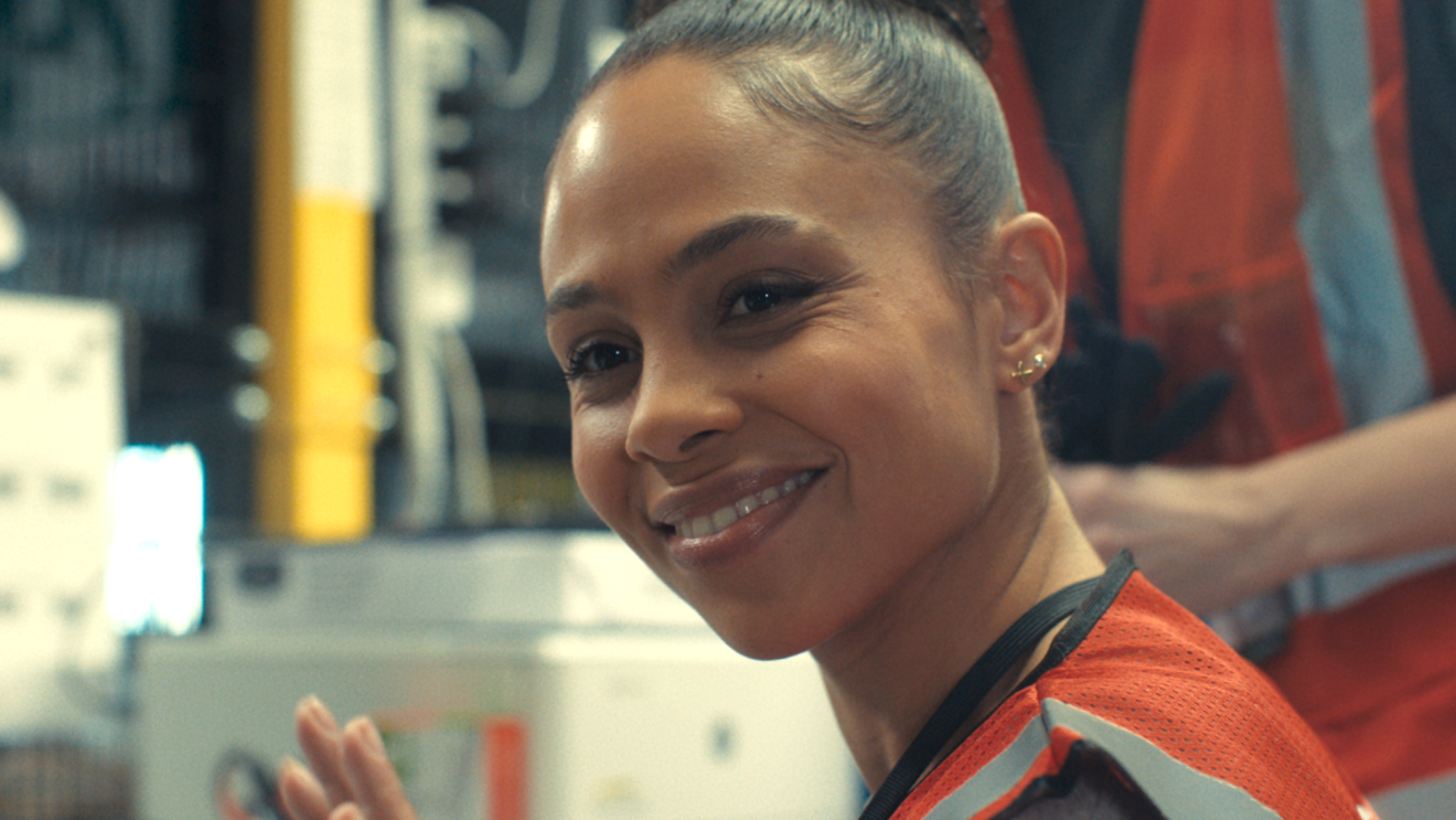 Eine junge Frau und Technikerin mit Sicherheitsveste lächelt.