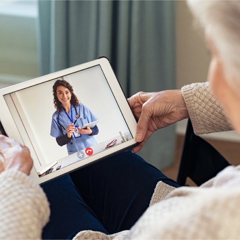 elderly person looking down at a tablet screen which shows a video of a clinician consulting during a health appointment