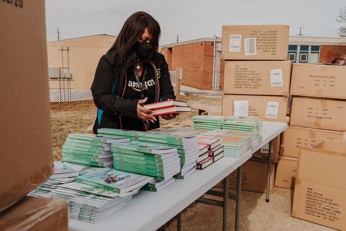 Nancy Dalton stacking books on a table while wearing a mask. There are boxes of books around her. 
