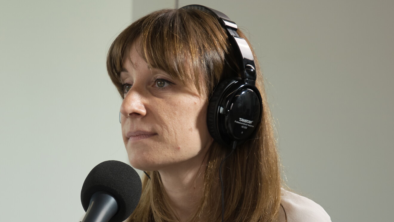Marie Mulot, responsable en el Marketplace de Amazon, sentada en una mesa delante de un micrófono y con unos auriculares puestos. Ella está mirando al infinito. Lleva el pelo largo suelto con el pelo castaño. Una camiseta blanca color blanco y un reloj negro.  