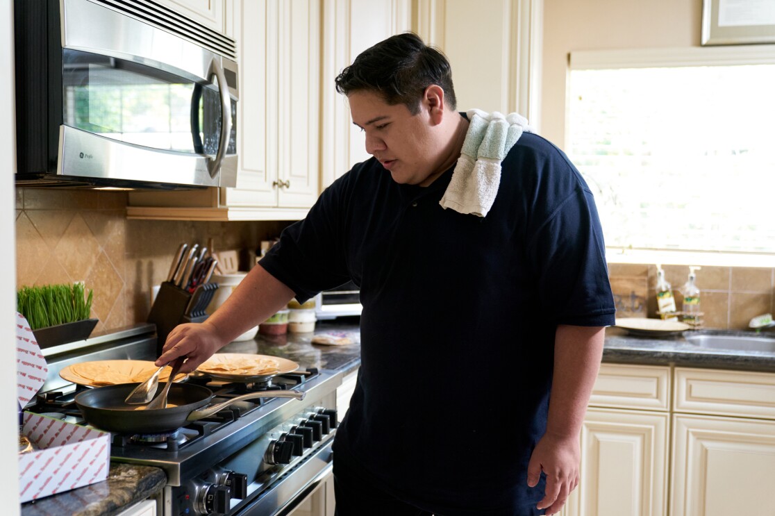 A man holding tongs cooks tortillas on a skillet.