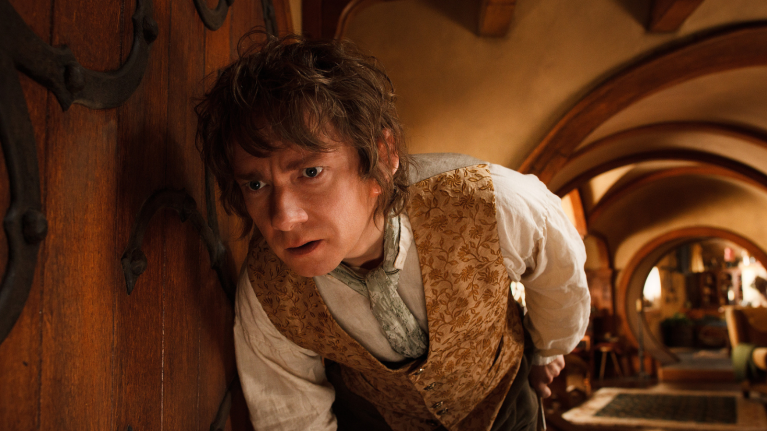 Hobbit in his home and dressed in a waistcoat looking around a door