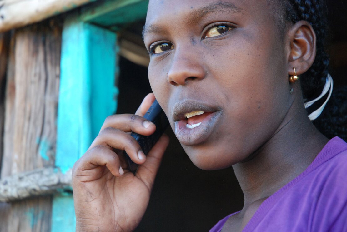 A close up image of a woman holding a phone up to her ear while speaking.