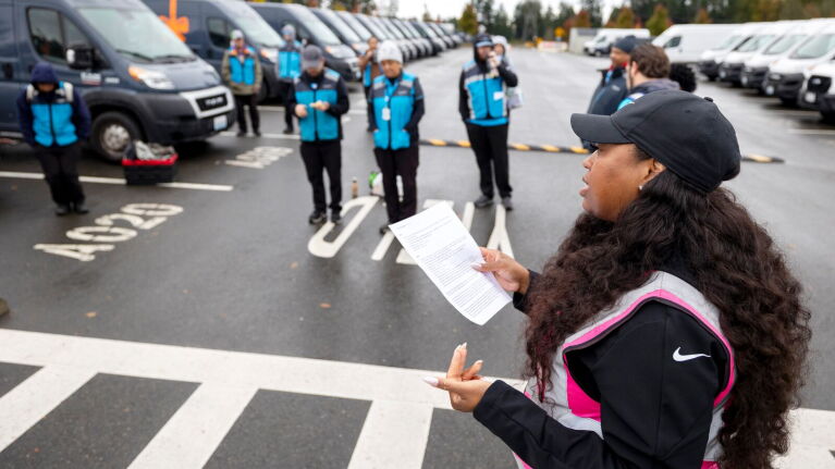 Amazon Delivery Service Partner addressing group of workers in blue vests in parking lot