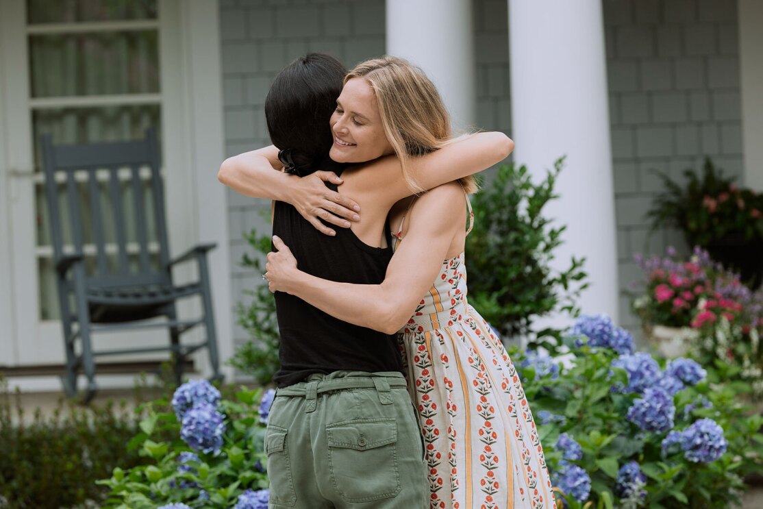 An image of Susannah and Laurel hugging in front of the beach home at Cousin's Beach. Susannah is smiling big while hugging Laurel.