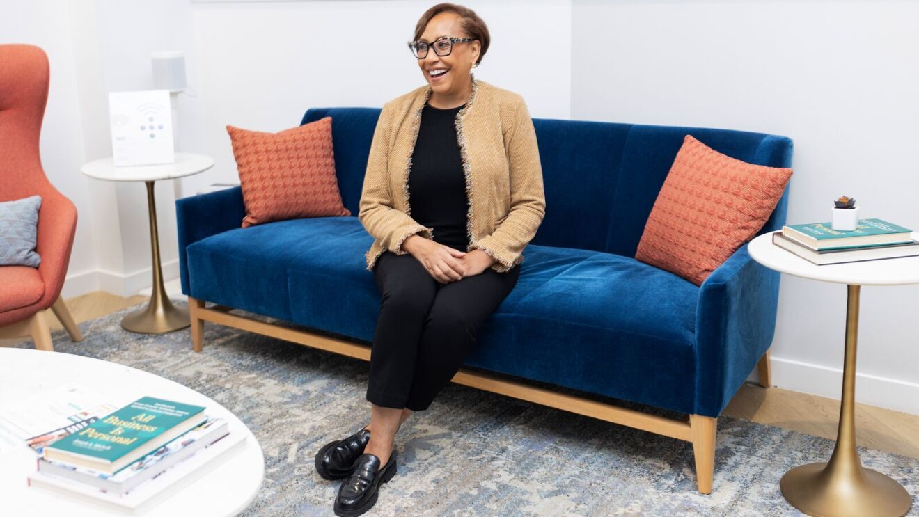 Leslie Meyers, Amazon One Medical patient, smiling on blue velvet couch with coral pillows in waiting room