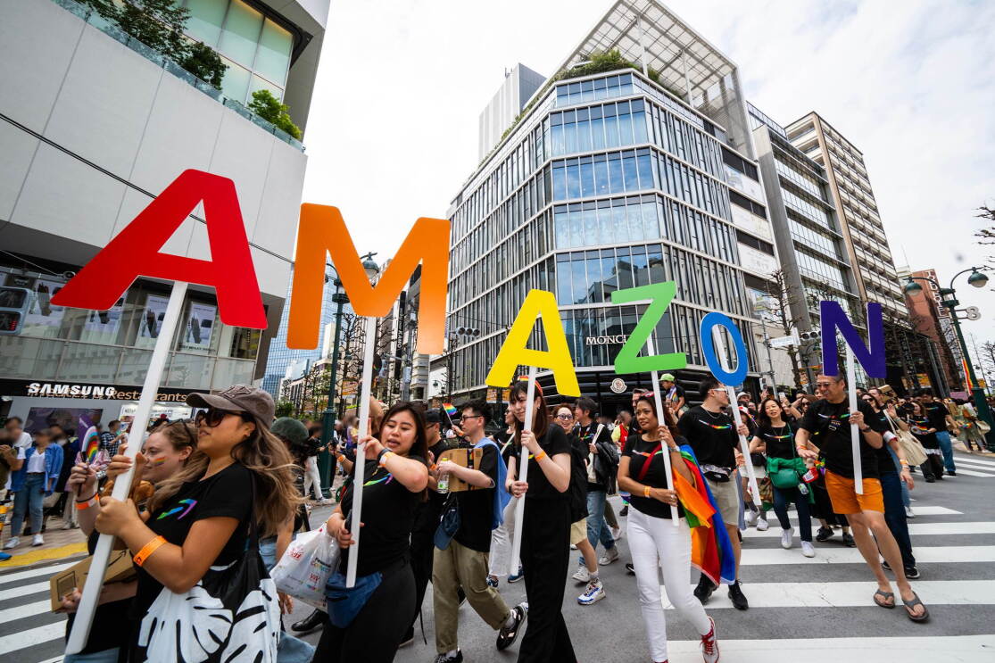 カラフルなAMAZONの1文字ずつの飾りを持って、交差点を歩いている人たち