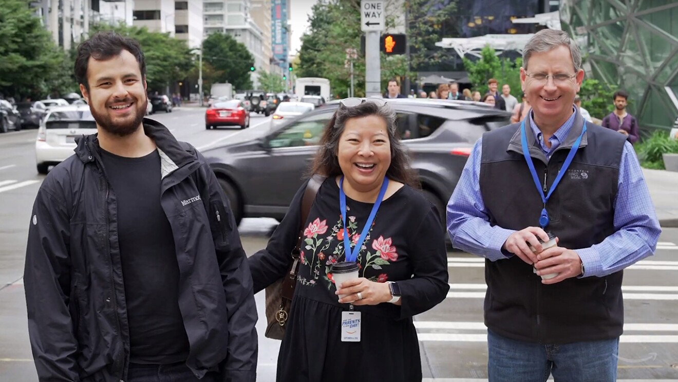 A man stands on the sidewalk next to his mother and father, on the Seattle Amazon campus.All are smiling and laughing.