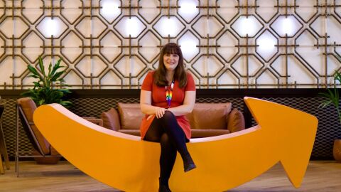 Cheerful employee relaxing on quirky yellow couch shaped as the Amazon smile in office lounge area