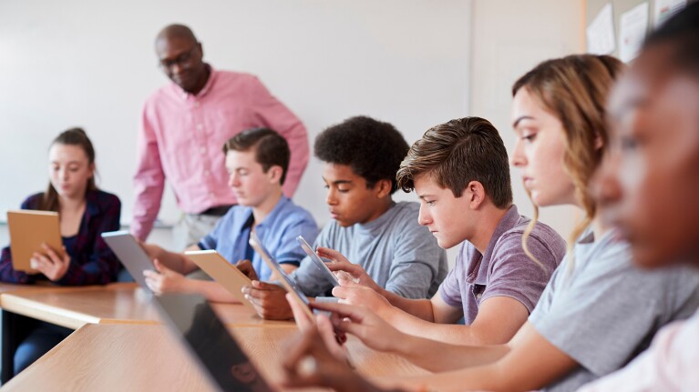 A photo of students in a class room reviewing content on tablet devices.