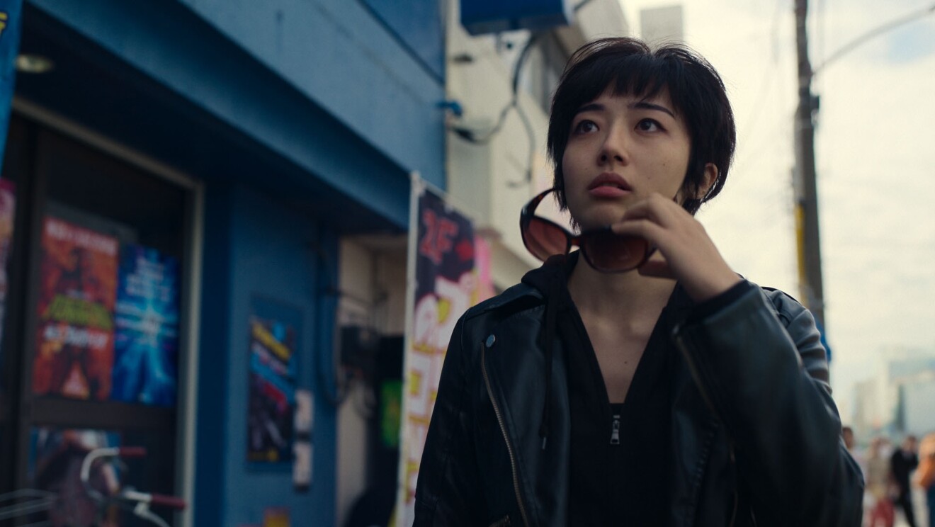 繁華街でサングラスを外し、上方を見つめるショートカットの女性