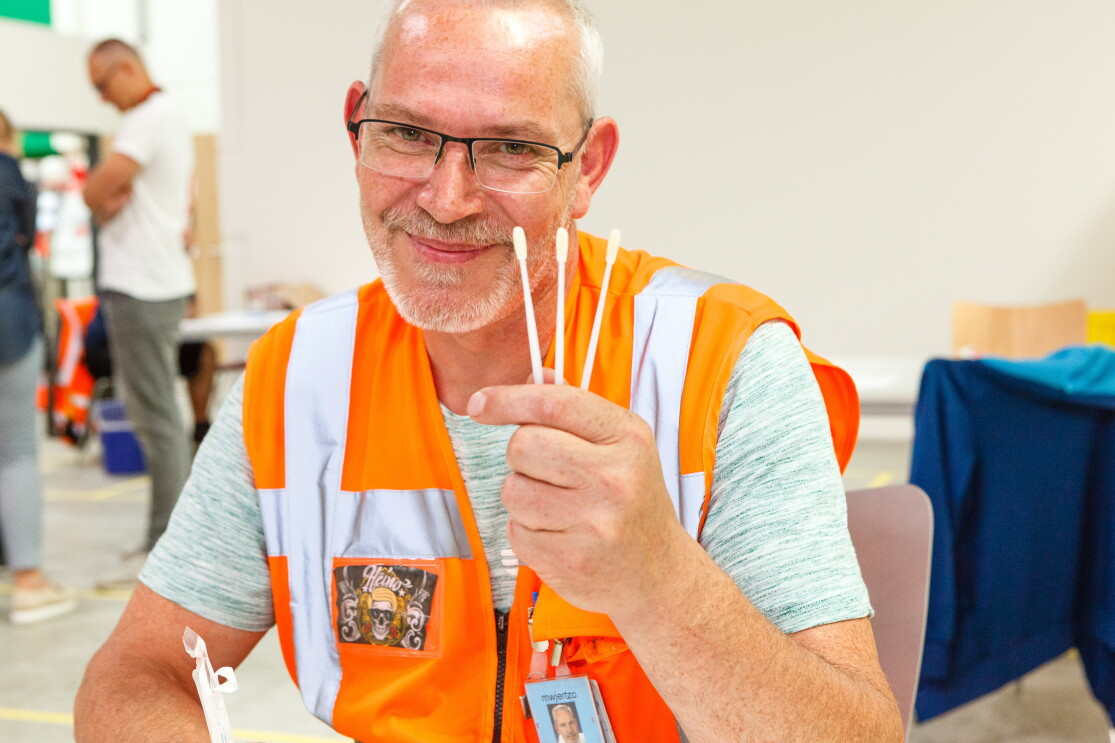 2 Männer mit Sicherheitsweste halten eine DKMS-Karte und ein Wattestäbchen