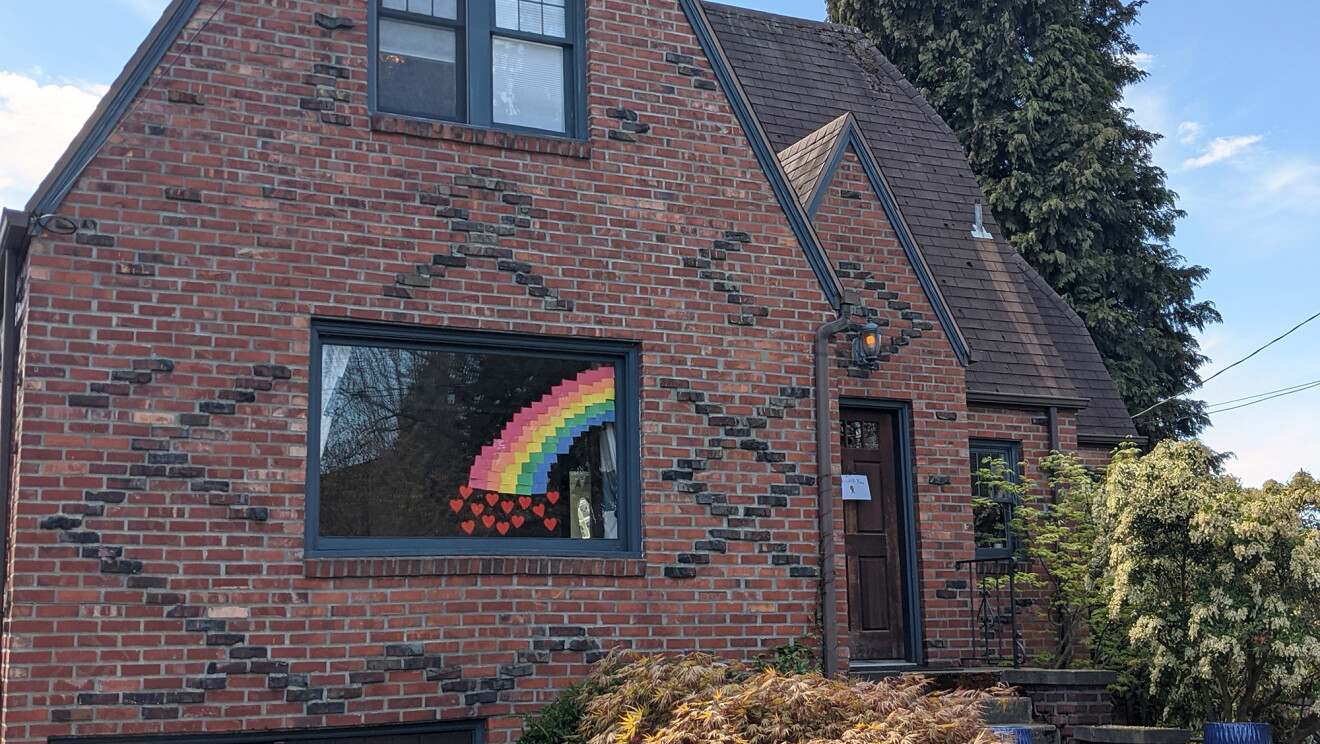 Rainbow in the front window of a brick Tudor-style home during COVID-19 pandemic.