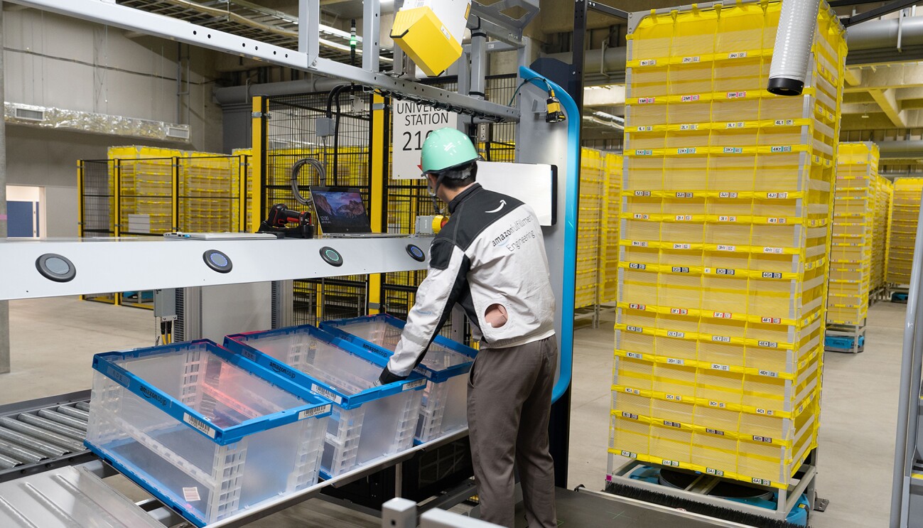 黄色い棚の前で作業をする男性。ヘルメットをかぶり作業服を着ている