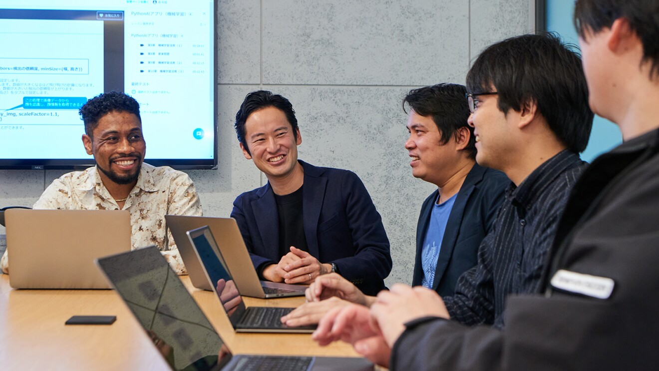 会議室で男性5人がにこやかに会話している