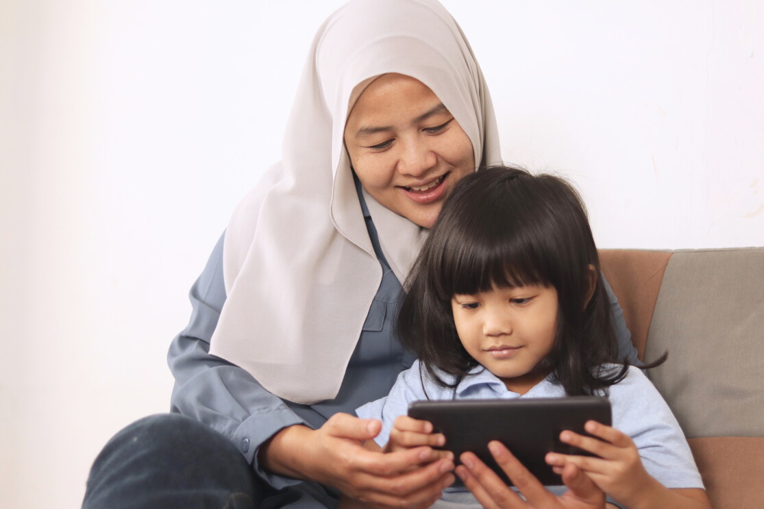 Mom sitting with her daughter using a tablet and smiling