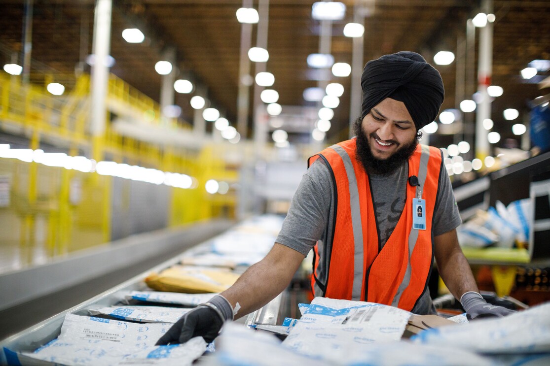 An Amazon associate wearing safety gloves and vest over his clothes, handles customer orders at an Amazon Fulfillment Center, BFI5 in Kent, Washington.