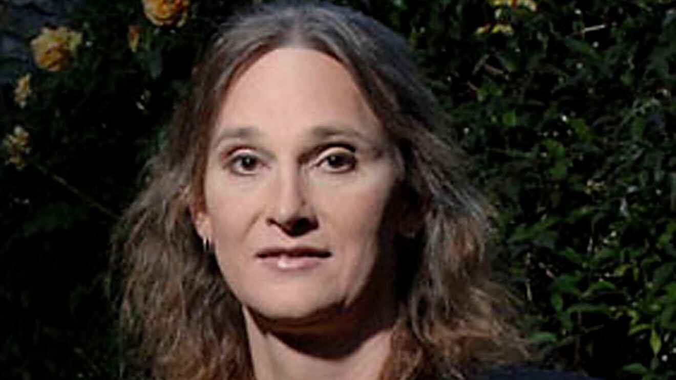 A headshot photo of Jessica Bussert smiling for a photo in front of a wall with greenery and yellow roses on it.