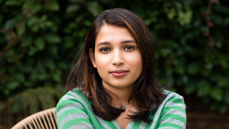 An image of Anjana Anand sat on a chair