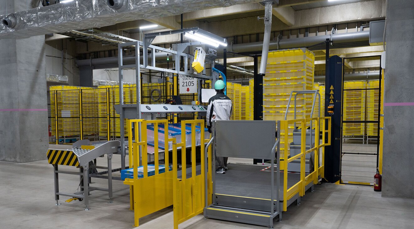 黒い金網のフェンスの手前に約2畳ほどの広さの作業スペースが設けられている。金網のフェンスの向こうにはARの黄色い棚が並んでいる