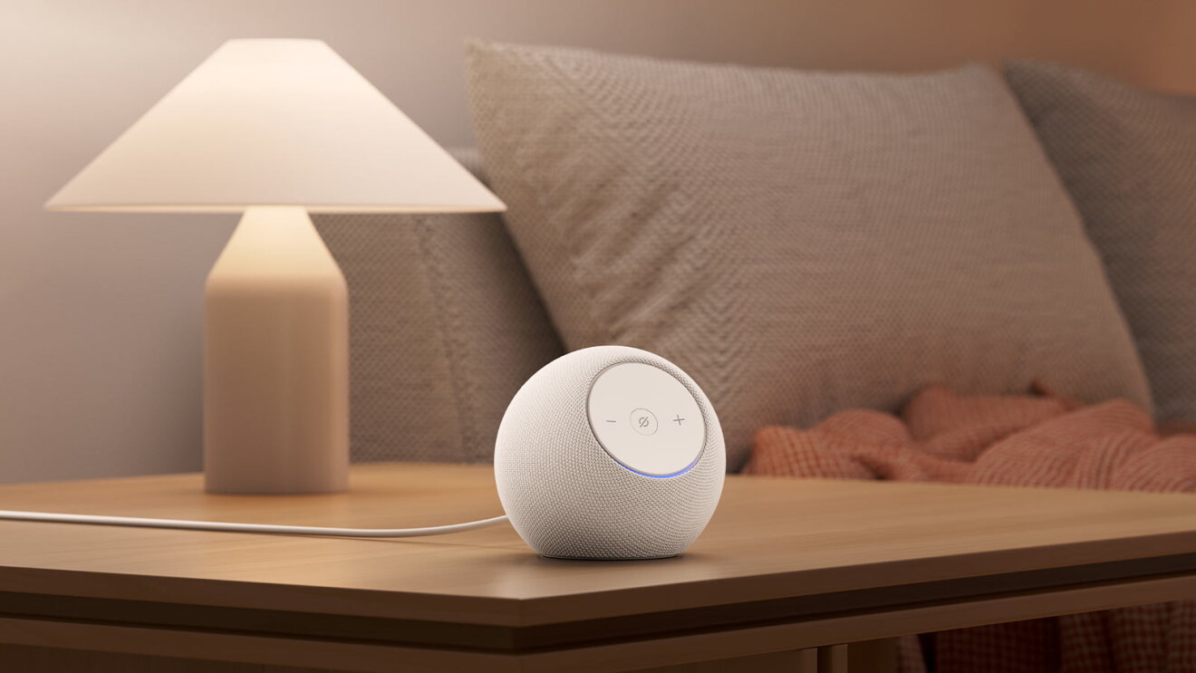 Echo Dot Max on a wooden table next to a lamp and beige couch