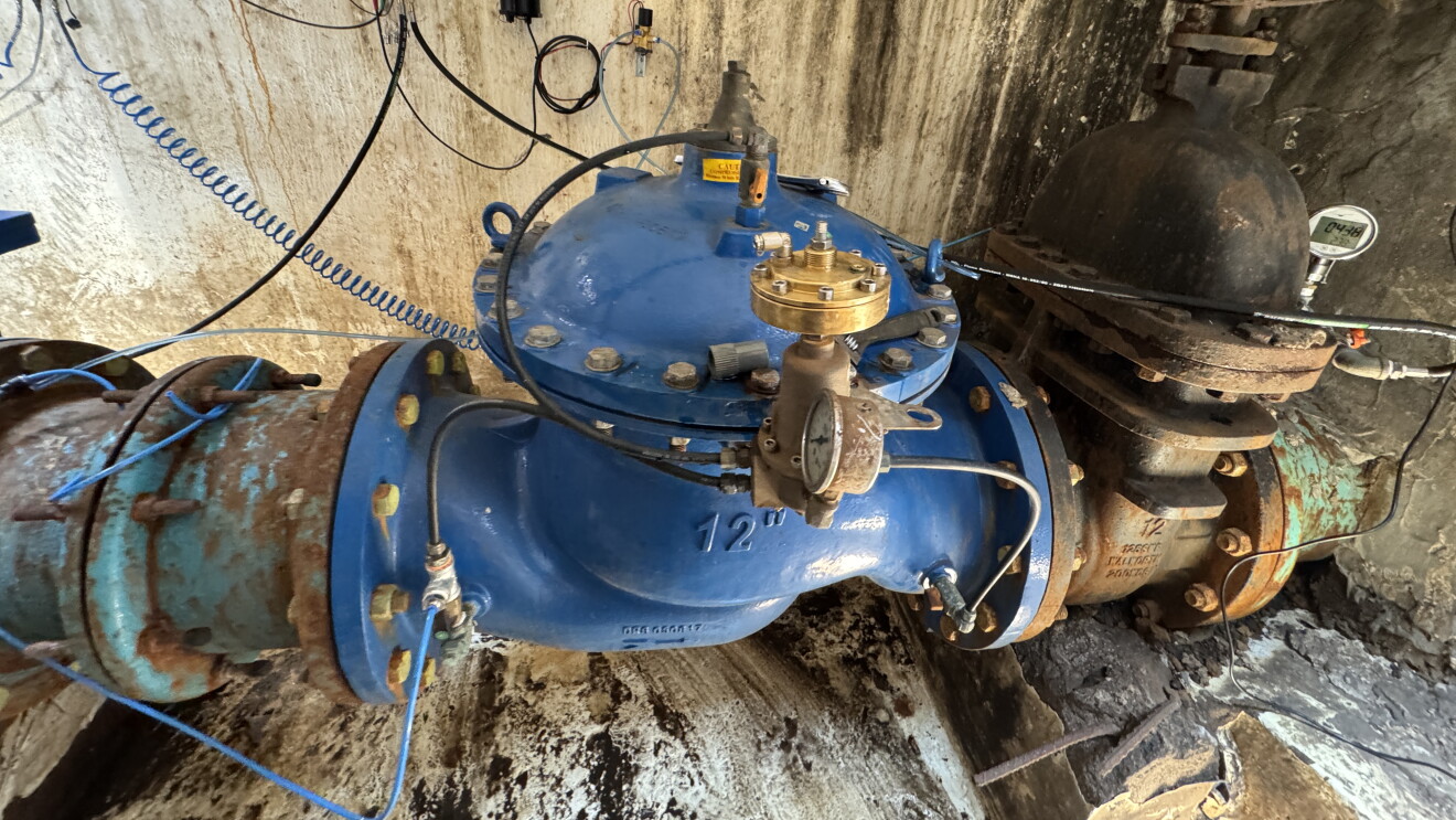 Large blue industrial valve with pipes and wiring in a concrete structure