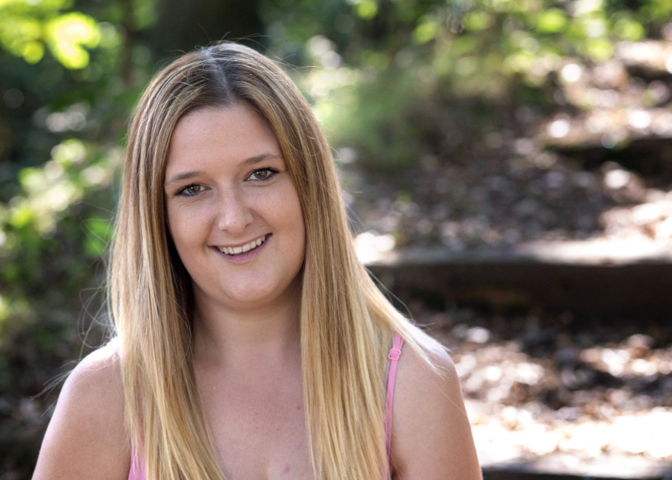 A headshot of Genna Holliss sitting in a woodland park.