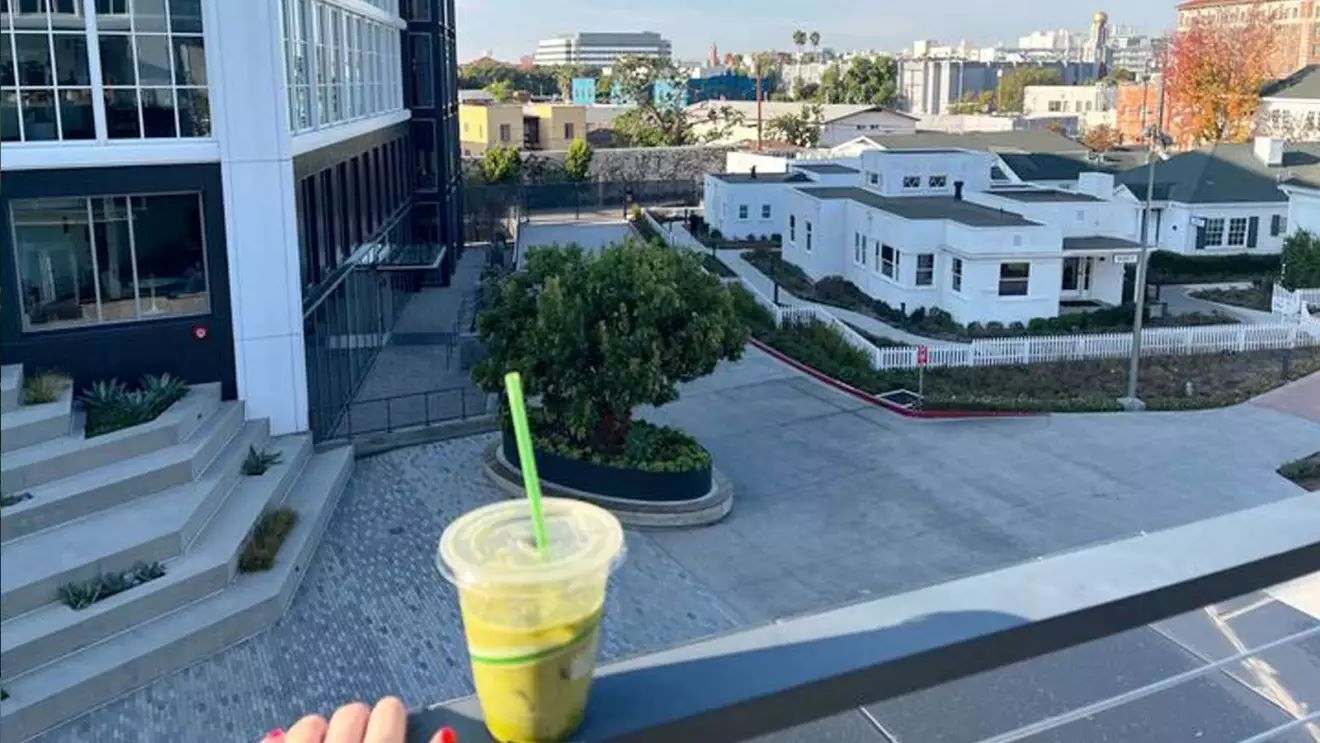 緑色のドリンクがバルコニーの手すりに置かれている。そのバルコニーから大きな白い家が見えている。