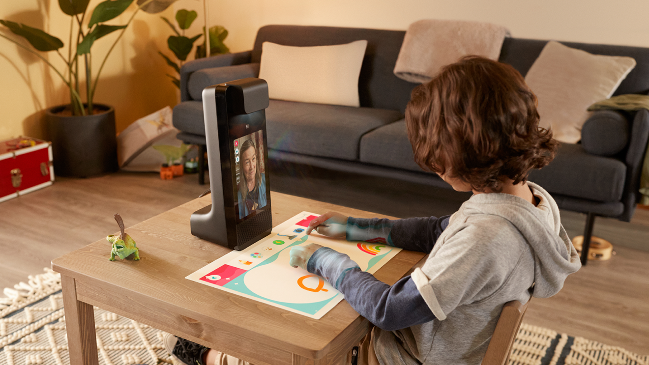 An image of a young boy drawing a digital drawing using an Amazon Glow device. A woman on the screen of the device smiles at him while they're on a video call.