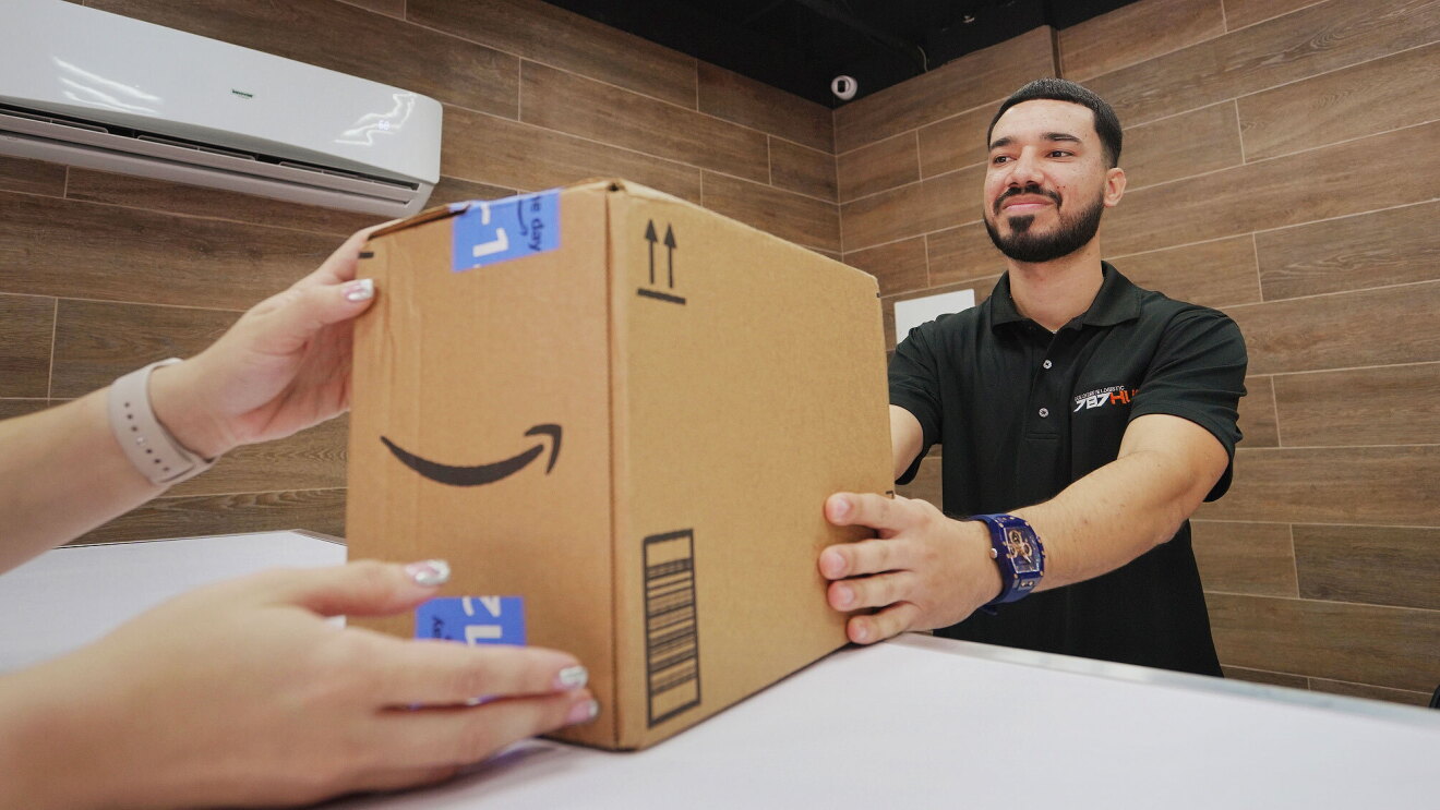 A person slides an Amazon package across a counter to a customer.