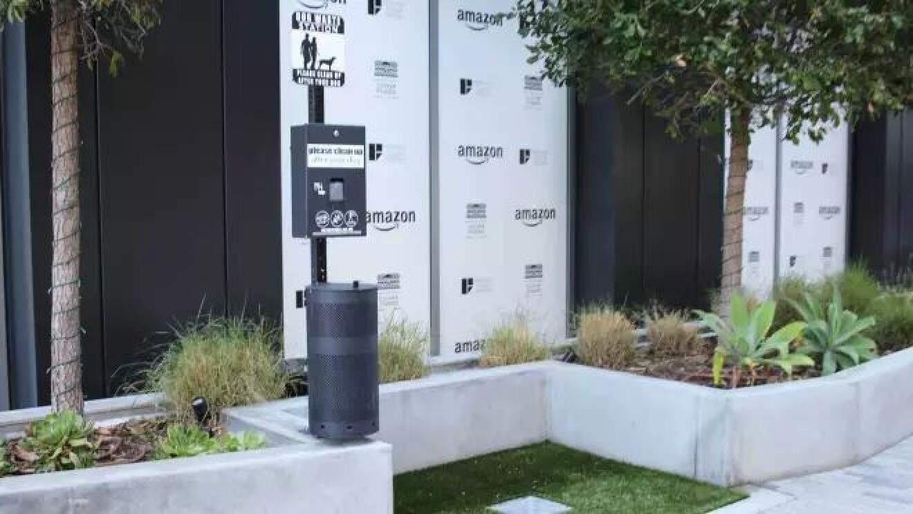 屋外のスペースの一部に人工芝がひかれていて、ゴミ箱などが置かれている。その横に人と犬を描いた標識がある