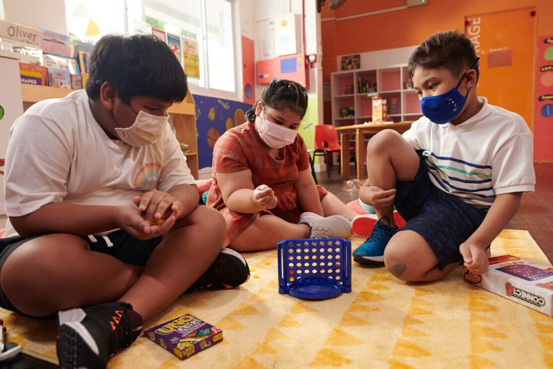 Children wear face masks and play with toys in a classroom-type setting