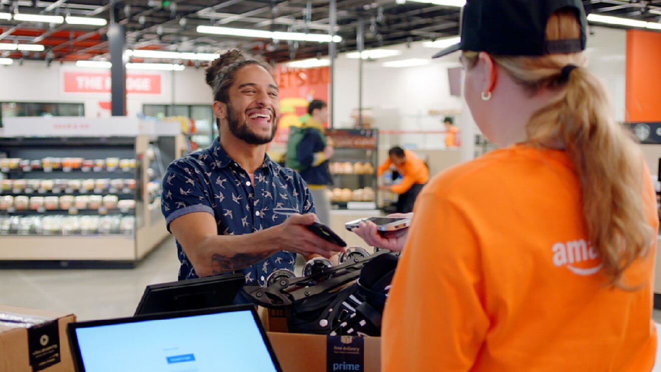 Prime Day 2023 live blog best deals: man smiling at an Amazon store associate at the checkout counter.