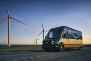 An Amazon Rivian van driving next to a wind farm during sunset. 