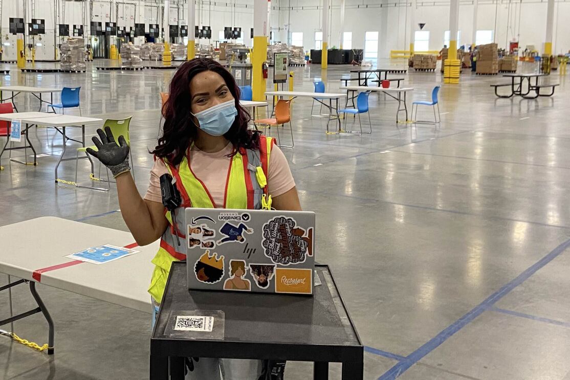 A woman wearing a safety vest and a mask works at a laptop computer.